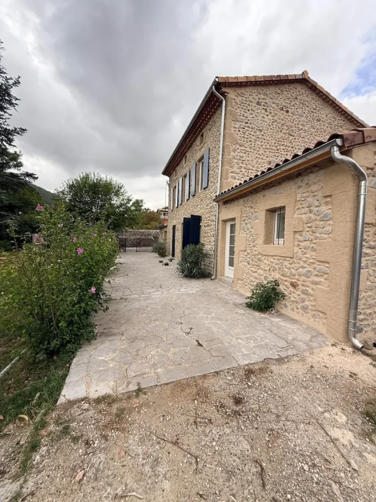 Cour pavée et façade sud de la maison en galets après travaux