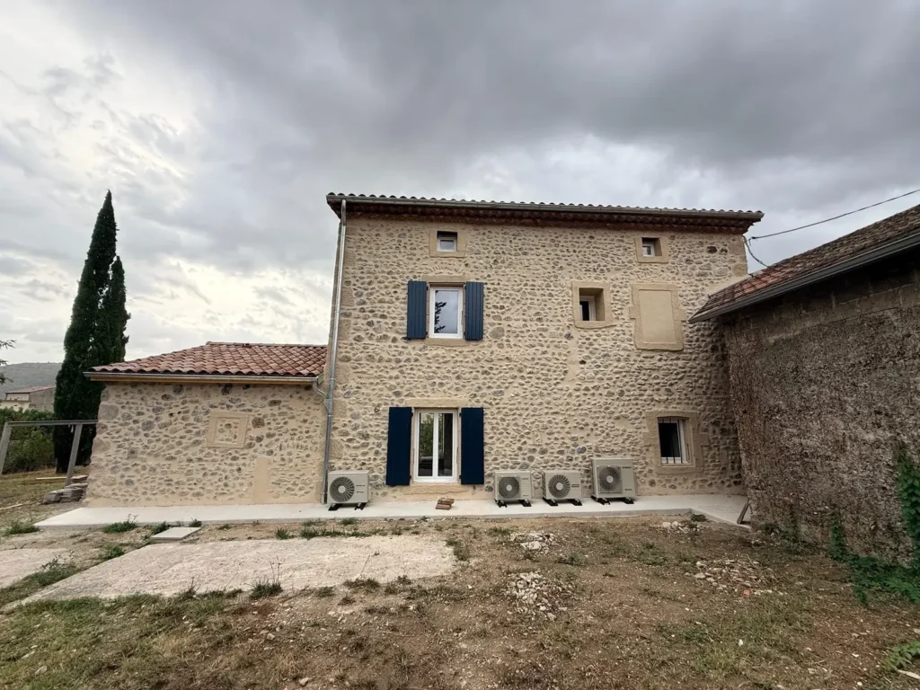 Façade nord de la maison en galets après rénovation, unités extérieures des pompes à chaleur