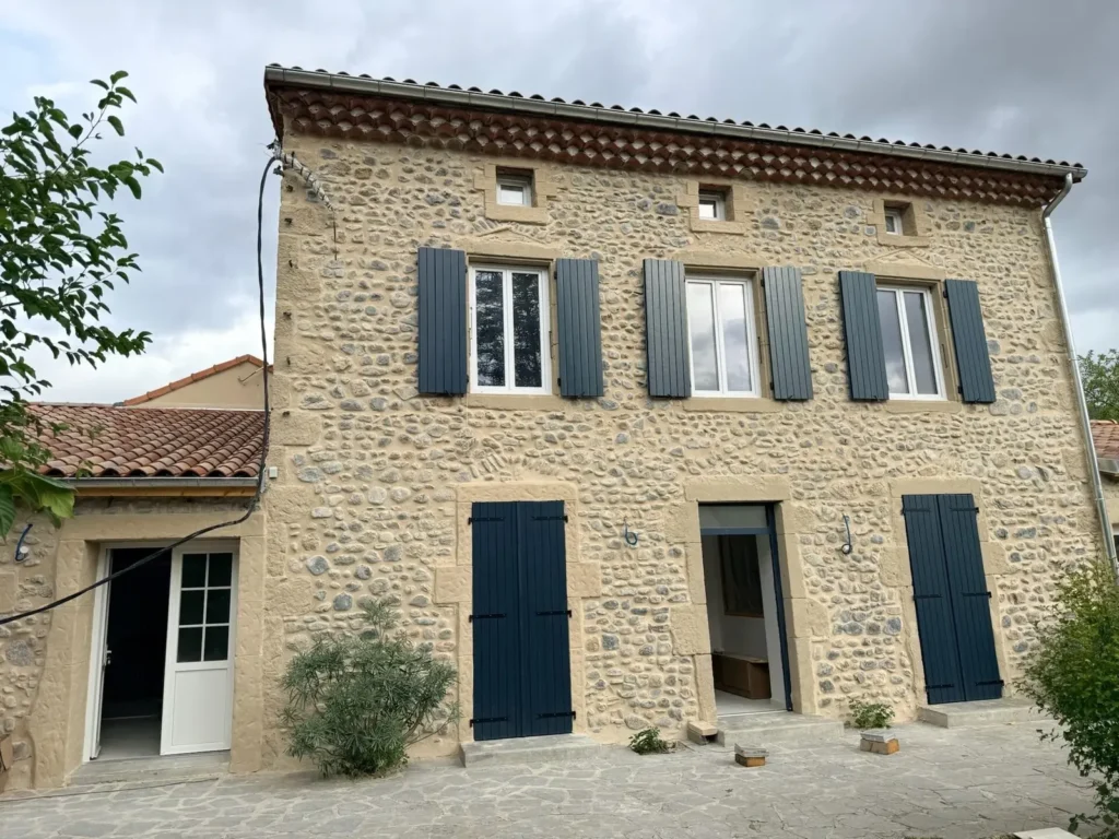 Façade sud de la maison en galets rénovée à Saint-Julien-en-Saint-Alban, volets bleu ardoise et encadrements en pierre de taille