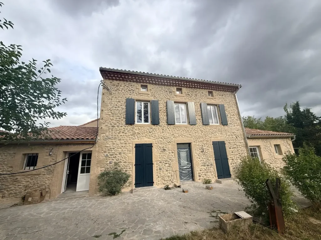 Façade principale en galets roulés après rénovation, enduit à la chaux et volets bleu ardoise
